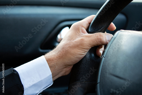 Close up Of A Man Hands Holding Steering Wheel While Driving Car. Businessman while driving, cropped. Driver's hand on steering wheel in suit. Guy sits in car and holds hands on steering wheel
