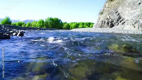 Shallow water flowing over stony riverbed under blue bky. photo