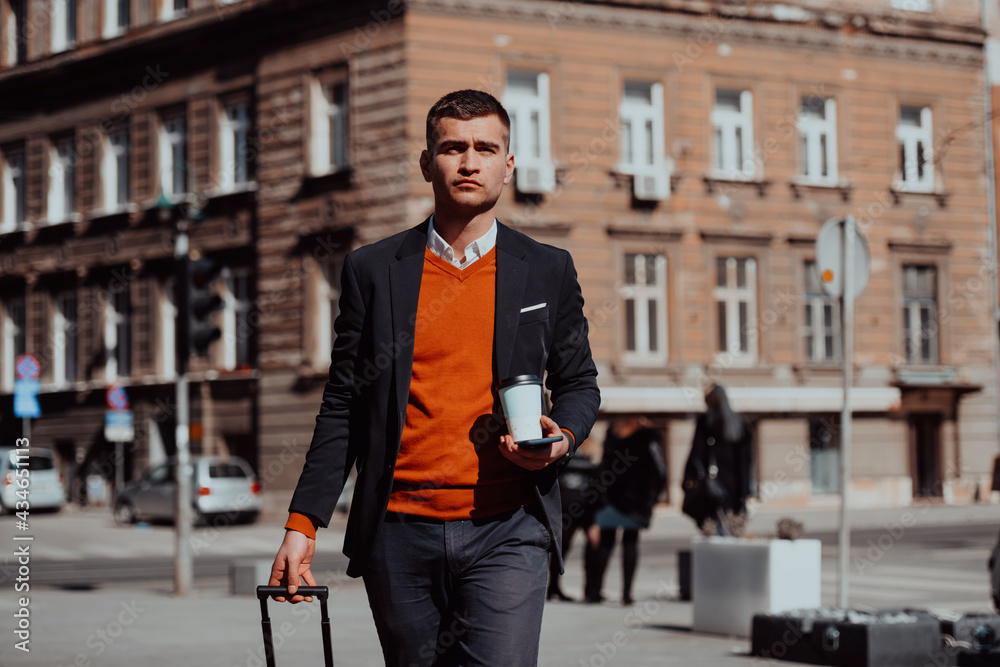 Going to airport terminal. Confident businessman traveler walking on city streets and pulling his suitcase drinking coffee and speaking on smartphone