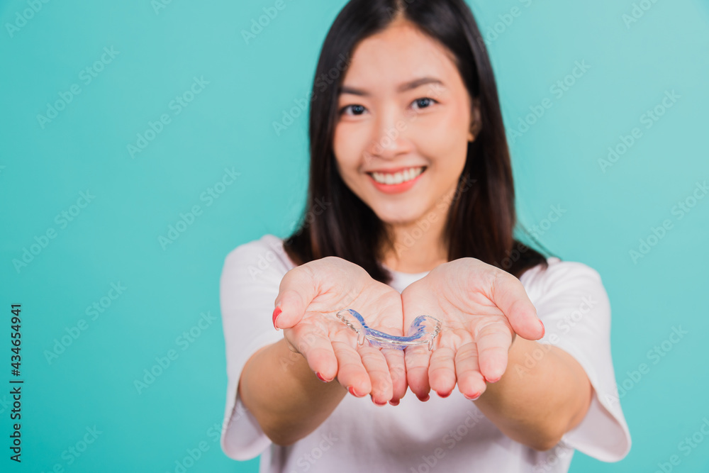Portrait young Asian beautiful woman smiling holding silicone orthodontic retainers for teeth on hand palm, Teeth retaining tools after removable braces, Orthodontics dental healthy care concept Portrait young Asian beautiful woman smiling holding silicone orthodontic retainers for teeth on hand palm, Teeth retaining tools after removable braces, Orthodontics dental healthy care concept