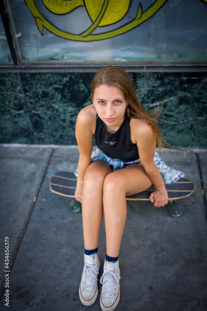 Down Angle Portrait of Teenage Girl Seated on Skateboard in San Jose