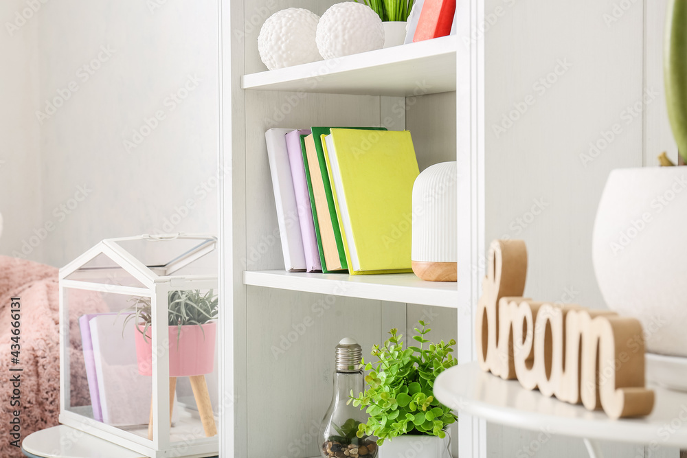 Fototapeta premium Shelf unit with books and houseplants in interior of light room, closeup