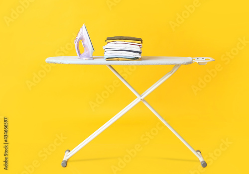 Photographie Board with electric iron and clean clothes on color background