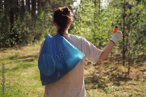 A volunteer collects plastic bottles in the forest. The girl holds a bag of garbage in her hands and shows a gesture with her hand: great, class. Concept call to protect the environment, the planet