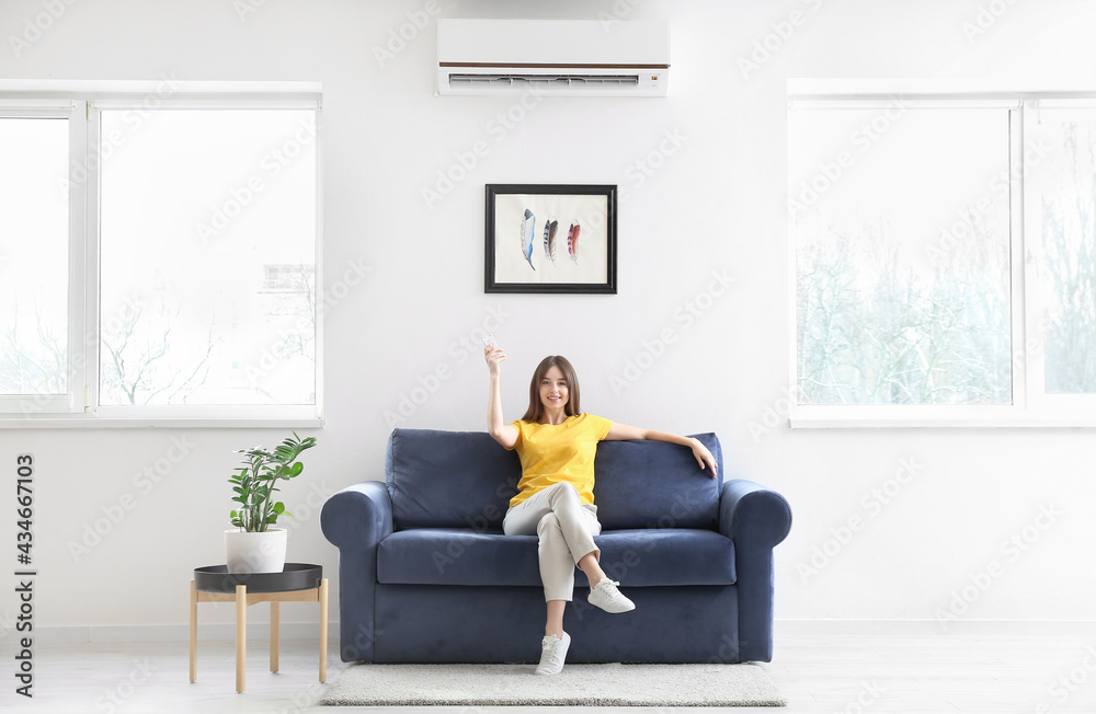 Young woman with air conditioner remote control at home Young woman with air conditioner remote control at home
