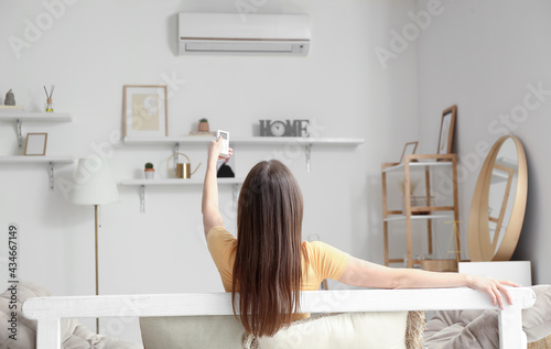 Young woman with air conditioner remote control on sofa at home photo