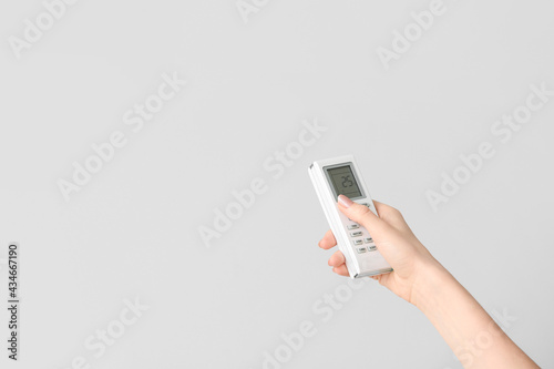 Young woman with air conditioner remote control on light background