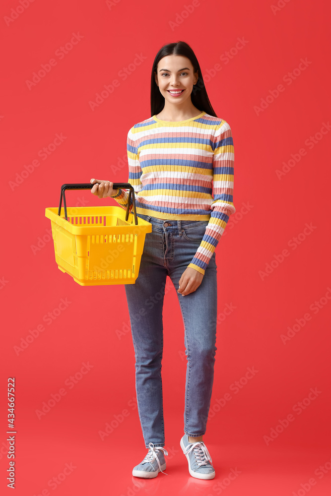 Naklejka premium Young woman with shopping basket on color background