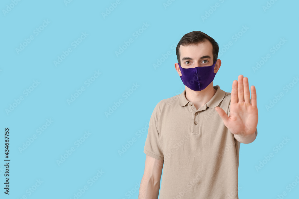 Young man wearing medical mask and showing STOP gesture on color background Young man wearing medical mask and showing STOP gesture on color background