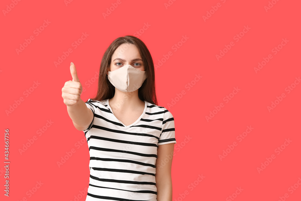 Young woman wearing medical mask and showing thumb-up on color background Young woman wearing medical mask and showing thumb-up on color background