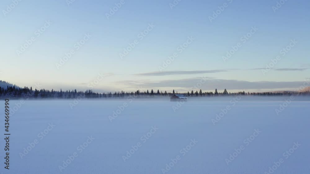 Drone flying over idyllic farmland with wooden farmstead located in snowy nature environment during dawn sunshine, snowscape with homestead hut during winter morning time in tranquil Wonderland