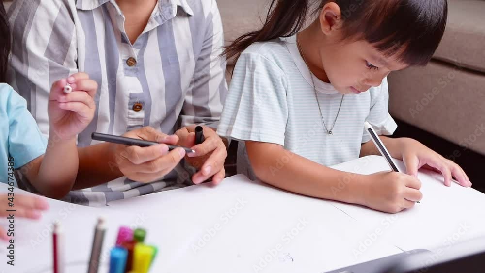 Happy mother and daughters learned to draw through the laptop computer in the living room. Mother helping the girls to draw a picture on paper. Home school concept. Kindergarten online classes. Happy mother and daughters learned to draw through the laptop computer in the living room. Mother helping the girls to draw a picture on paper. Home school concept. Kindergarten online classes.