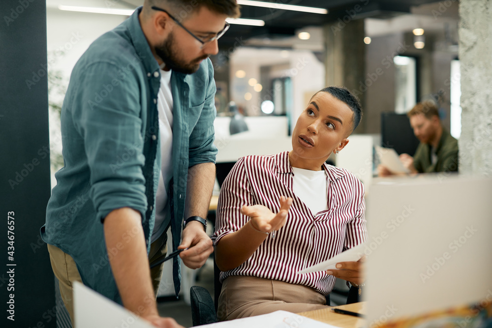 Young black entrepreneur discussing about business reports with her coworker in the office.