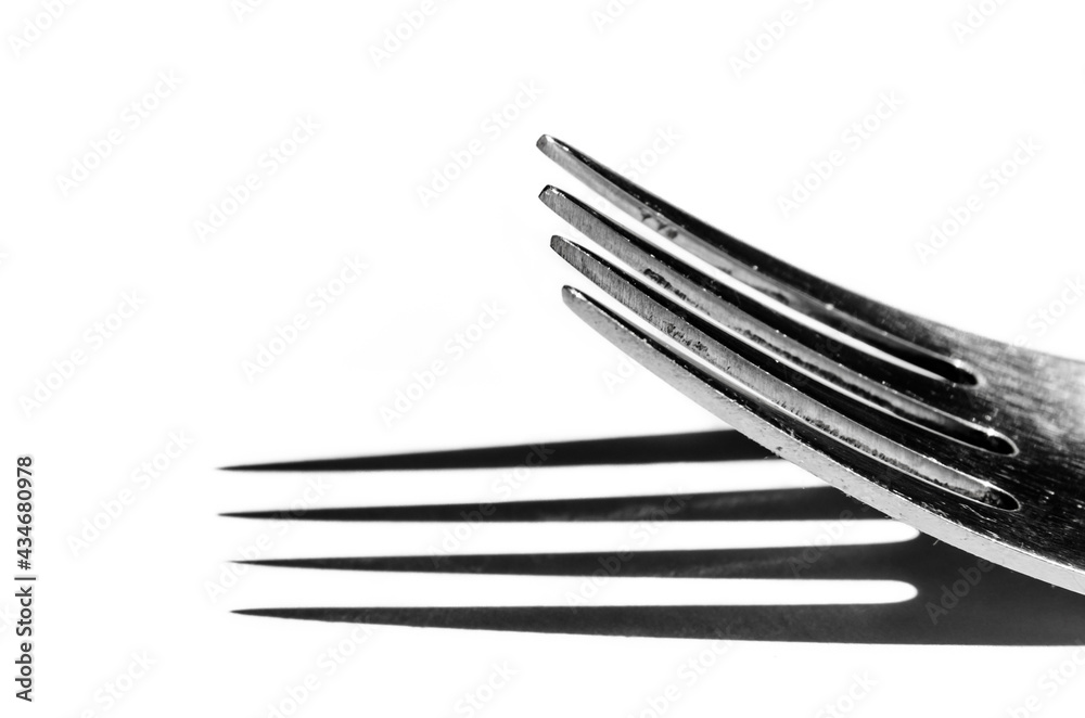 Closeup of a fork horizontally on a white surface, with a harsh shadow Closeup of a fork horizontally on a white surface, with a harsh shadow