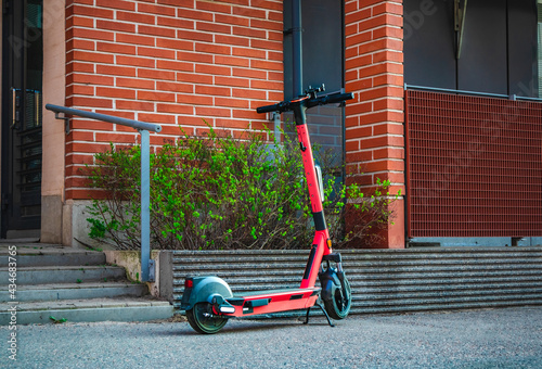 Electric kick scooter for rental parked on sidewalk of street in front of brick wall building. E-scooter for public sharing in European city center. Urban Transportation Concept. Rent eco transport.
