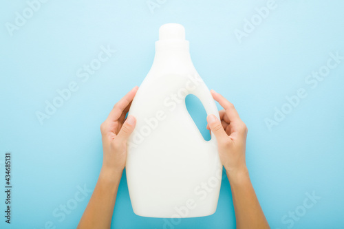 Young adult woman hand holding white 5L plastic container on light blue table background. Pastel color. Cleaning detergent, washing liquid or body care product. Empty place for text or logo. Top view. photo