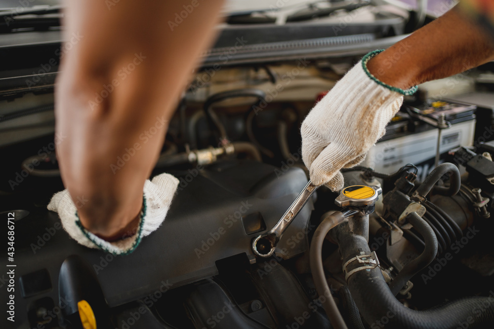 Hand of an auto mechanic is repairing the problematic car. He was wearing white cloth gloves, holding a wrench. Hand of an auto mechanic is repairing the problematic car. He was wearing white cloth gloves, holding a wrench.