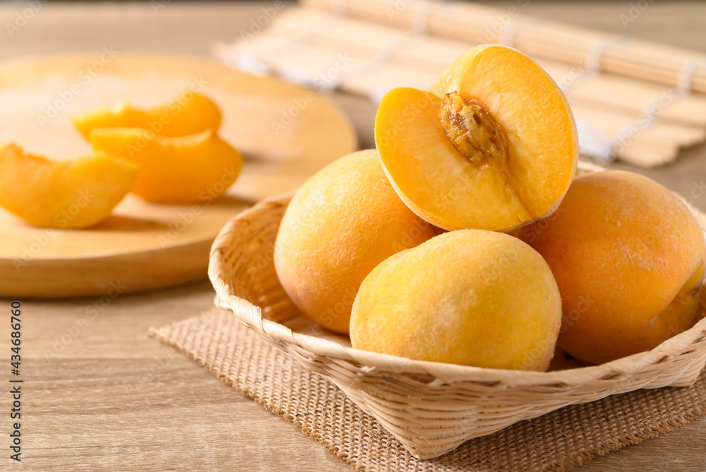 Yellow peaches in a bamboo basket on wooden table