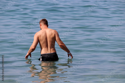 Muscular man going to swim in sea water, back view. Beach vacation and swimming