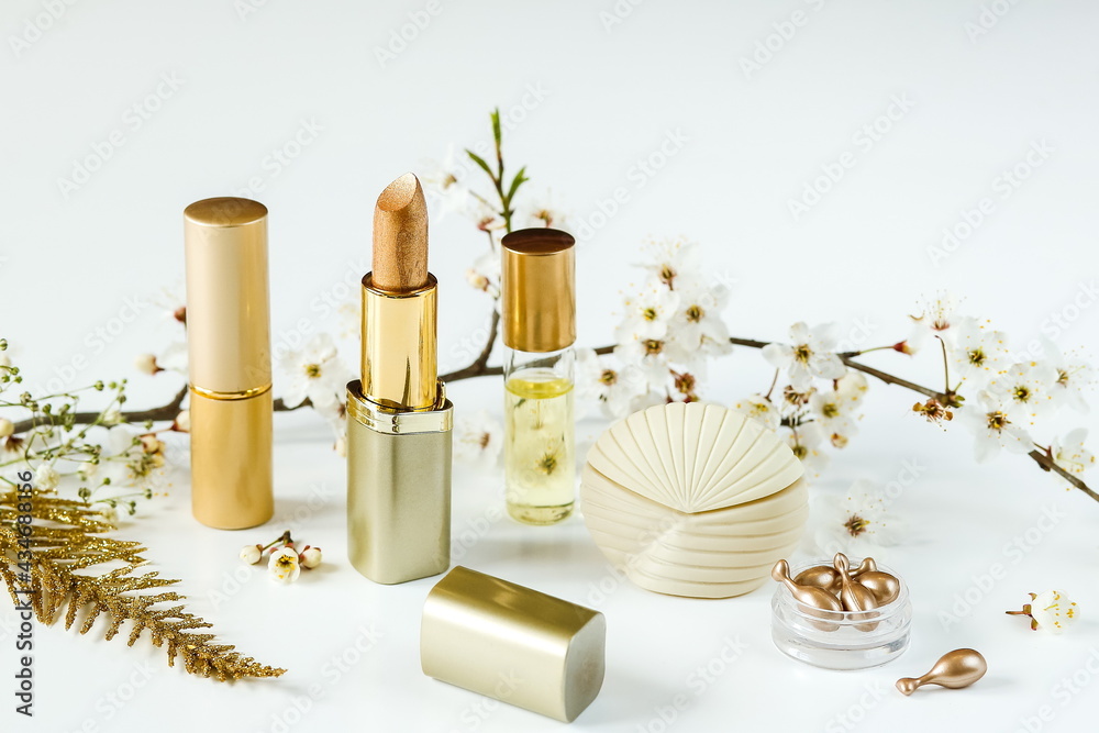 cosmetics in gold tones. lipsticks and scented oil and perfume on the background of a flowering branch