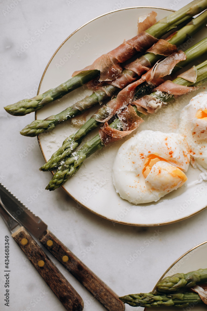 asparagus with boiled poached eggs. boiled green asparagus garnished with prosciutto or ham. healthy and tasty breakfast with asparagus. snack with asparagus top view.