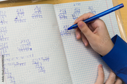 A girl's hand with a ballpoint pen writes in bad handwriting close-up. The student completes the task. A student solves examples in mathematics at school at a desk. Warm soft daylight.