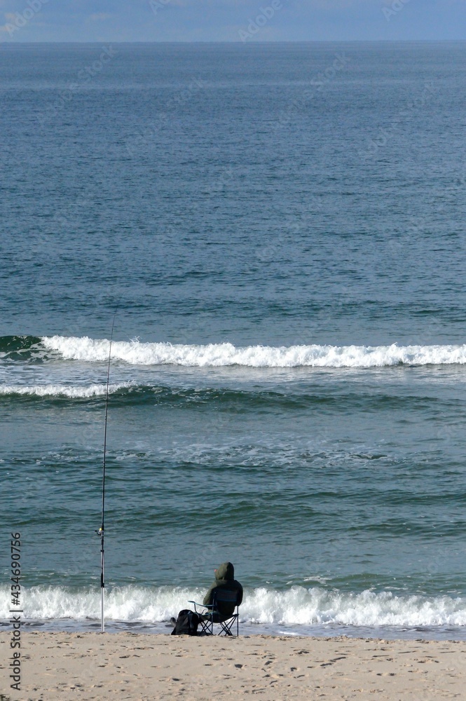 the angler is sitting on the beach next to the fishing rod, wondering if he will catch something