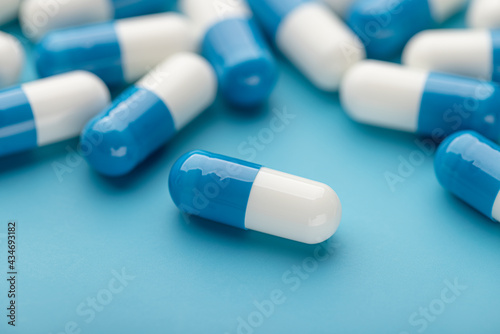 Double white and blue capsules. Pills on a blue background, close-up, copy space. Medicine concept, pharmacy.