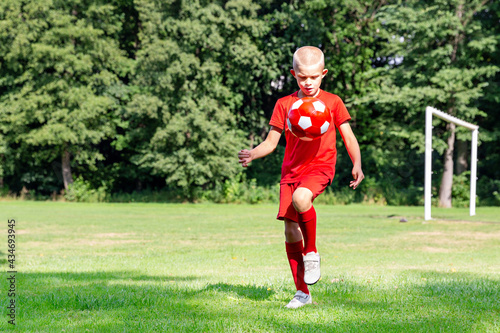 A boy in a red uniform hits a ball, does exercises, trains on the football field. Children's sports, physical activity concept