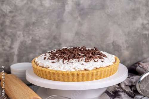 Homemade Banoffee pie with caramel, banana and chocolate topping on white cake stand.