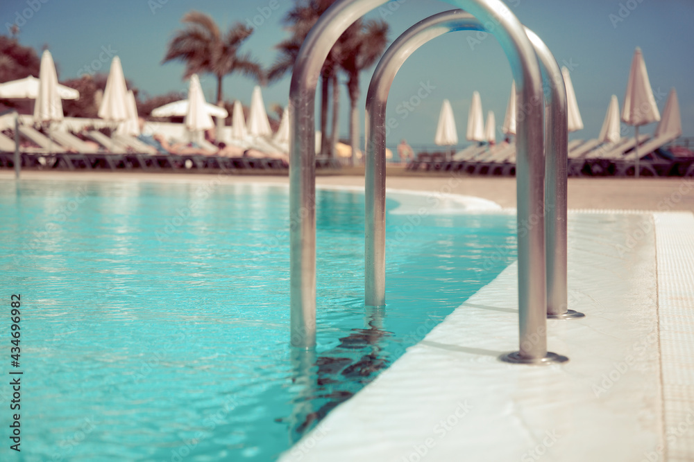 Hotel swimming pool side with blue water, close-up shot, with sunbeds on background