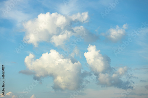 Vibrant soft blue sky with a couple of fluffy cumulus clouds floating lit by sunset light nicely in the middle of the frame