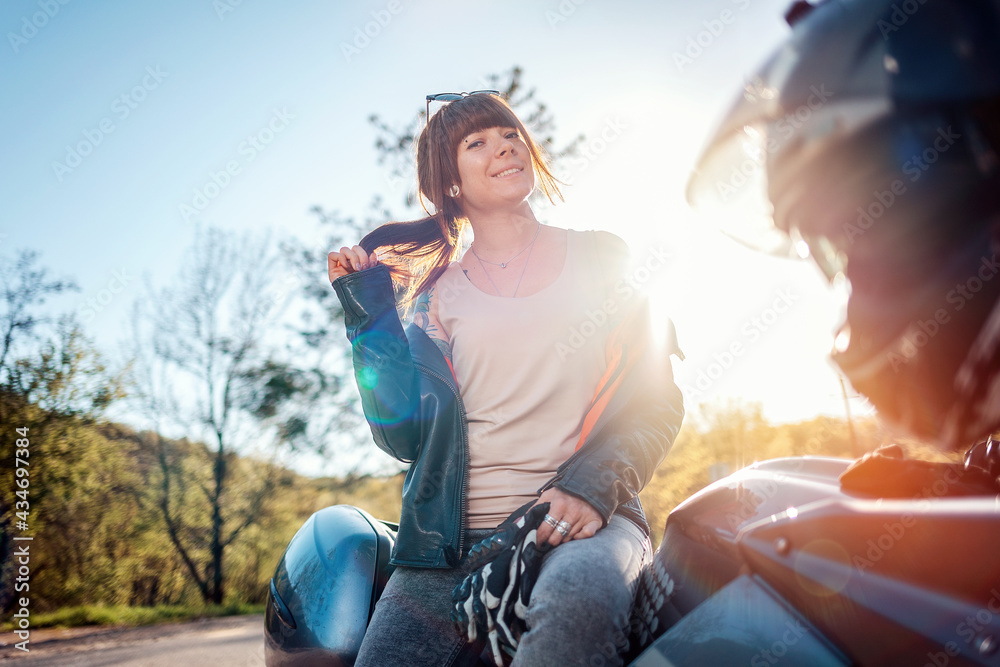 World Motorcyclist Day. A young smiling woman in a leather jacket, holding motorcycle gloves and sitting on a motorcycle. Motorcycle local travel concept