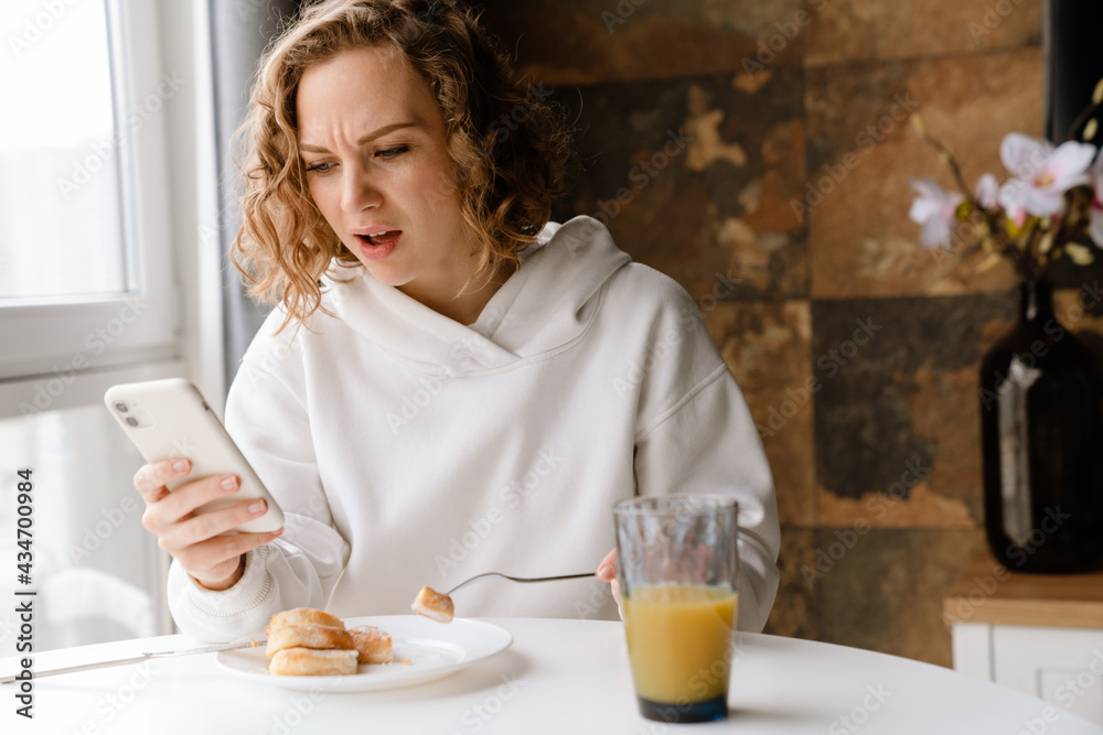 Young white woman using mobile phone while having breakfast at home Young white woman using mobile phone while having breakfast at home