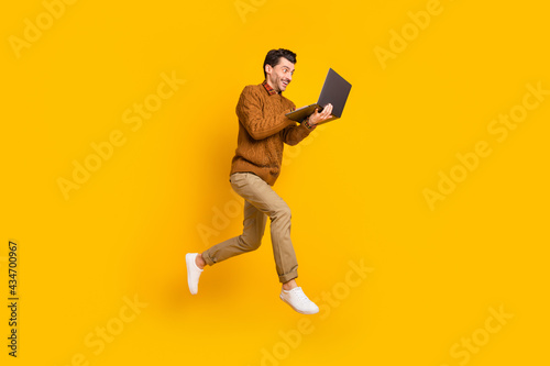 Full body profile portrait of cheerful energetic man running use laptop isolated on yellow color background