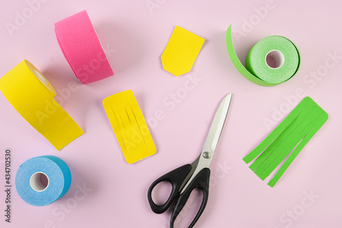 Colorful kinesiology tape, scissors and different shape cuts for applique on pink background. Kinesiology taping lymph outflow and speeds up the healing process.