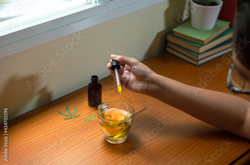 Woman pouring CBD tincture in a hot drink, natural medicine made with marijuana.