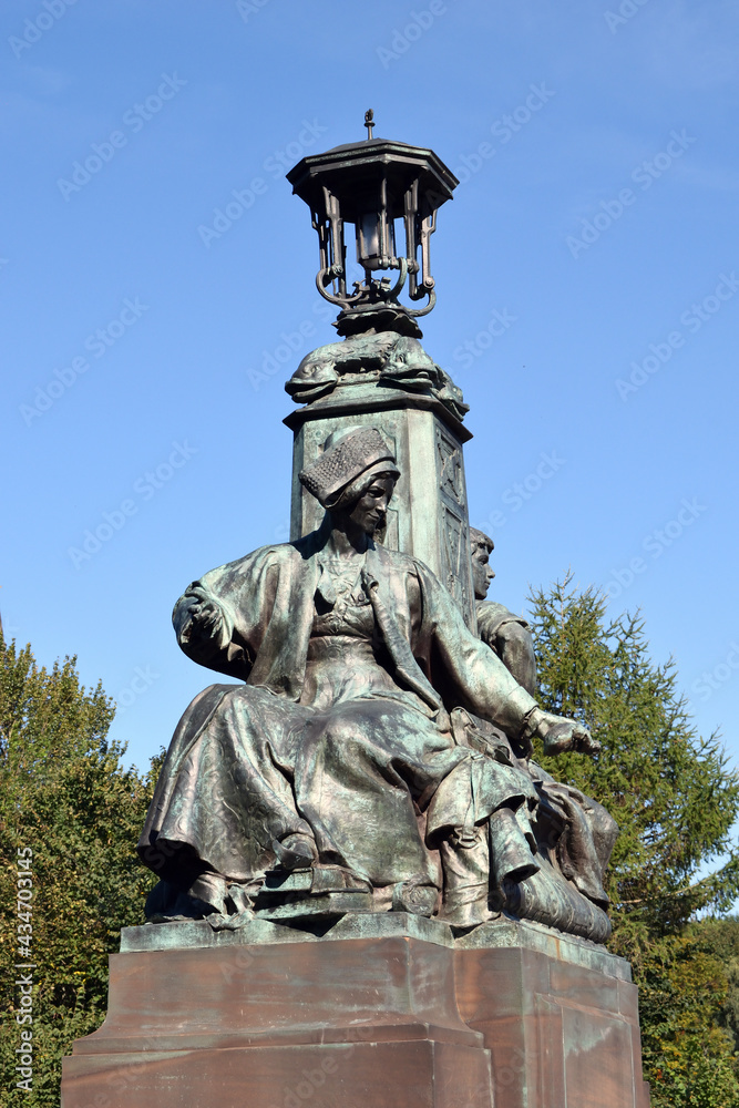 Sculpted Female Figure and Ornate Victorian Lamp against Blue Sky 