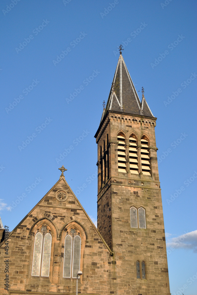 Fototapeta premium Stone Church with Gable-Tower & Spire seen from below against blues Sky 