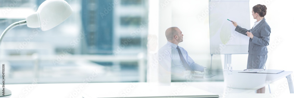 Composition of office desk with lamp over businesswoman giving presentation in office