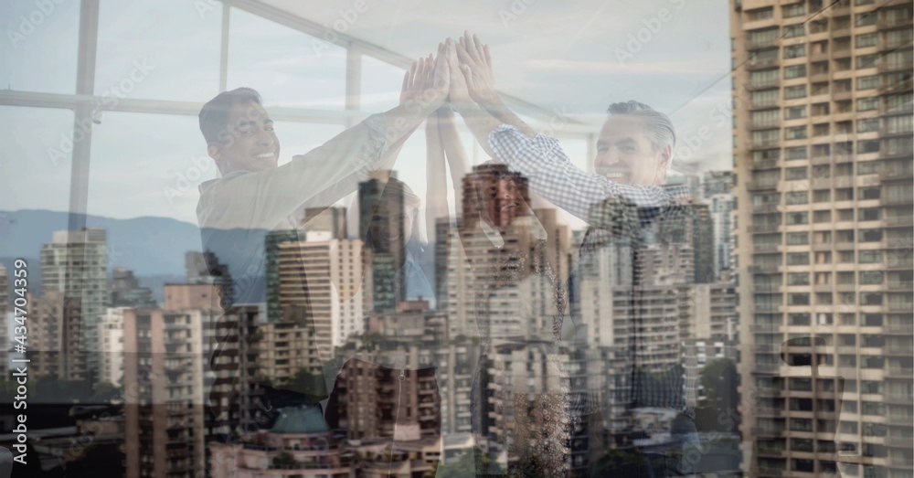 Obraz premium Composition of smiling office colleagues high fiving over cityscape