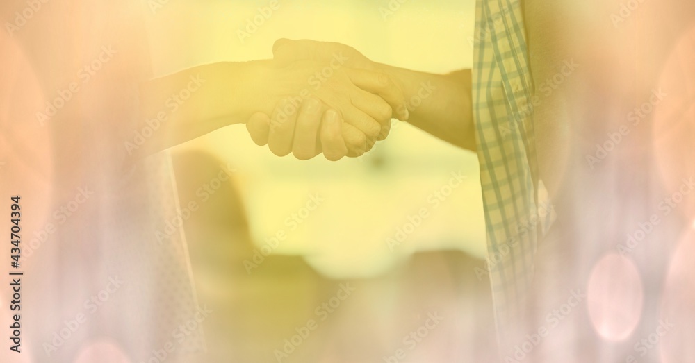 Composition of handshake with glowing yellow spots of light