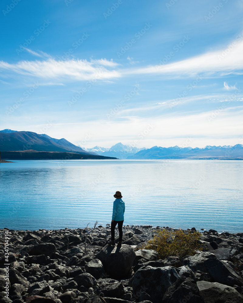 Woman standing on the shore of Lake Pukaki, enjoying the views of Mt Cook and Southern Alps, South Island. Vertical format.