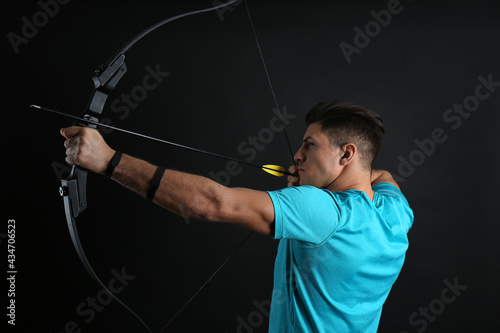 Man with bow and arrow practicing archery on black background