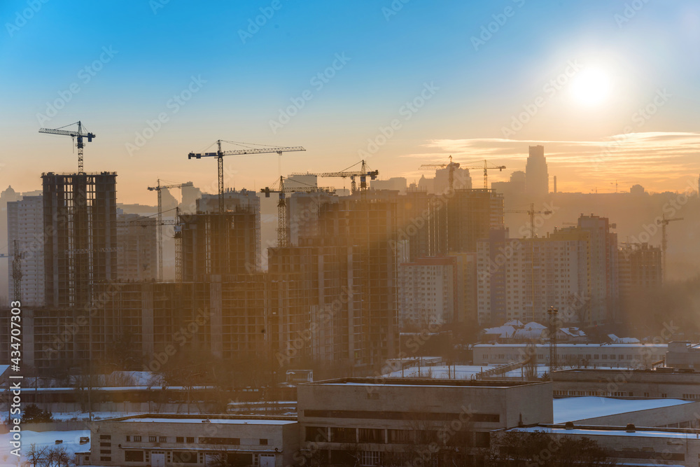 Construction site with industrial cranes in city at sunset