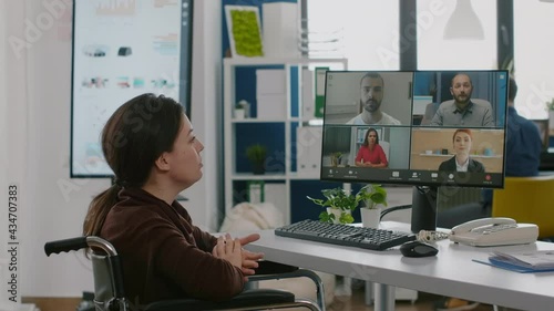 Paralyzed immobilized manager woman speaking online with remotely coworkers sitting wheelchair in start up busineess office at computer. Handicapped employee talking on virtual meeting photo