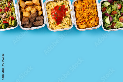 Take away healthy food in foil boxes on blue background. Copy space