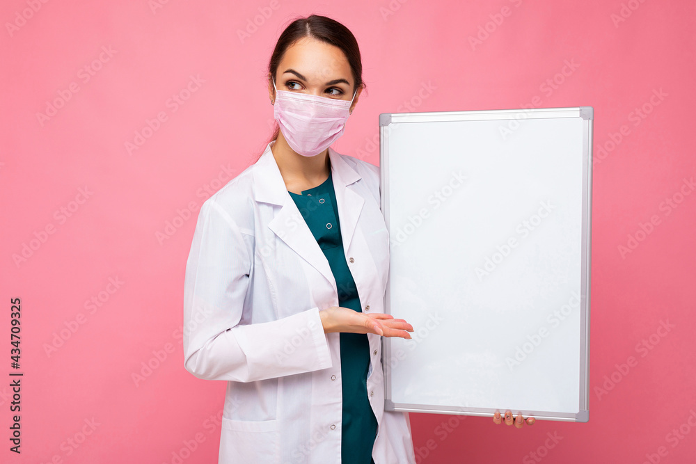 Woman doctor wearing a white medical coat and a mask holding blank board with copy space for text isolated on background. Coronavirus concept Woman doctor wearing a white medical coat and a mask holding blank board with copy space for text isolated on background. Coronavirus concept