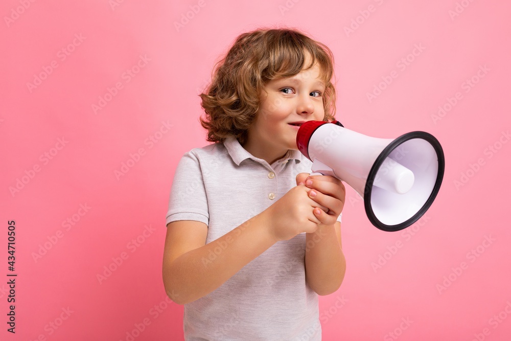 Photo of little handsome positive funny joyful happy smiling curly blonde boy with sincere emotions wearing t-shirt isolated over pink background with copy space and speaking into magaphone to Photo of little handsome positive funny joyful happy smiling curly blonde boy with sincere emotions wearing t-shirt isolated over pink background with copy space and speaking into magaphone to