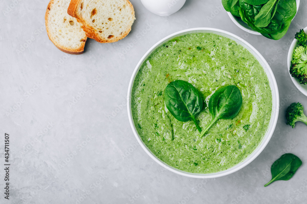 Green creamy spinach and broccoli soup with baguette toasts on a gray concrete background. Green creamy spinach and broccoli soup with baguette toasts on a gray concrete background.